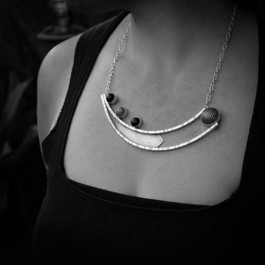 Black and white close up of woman's neckline. She is wearing a black shirt and a handmade modern geometric silver pendant.