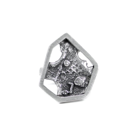 Modern brutalist inspired sterling silver ring featuring a single, asymmetric hexagon framing a blackened, melted, and fused texture backplate. View of front of ring on white background
