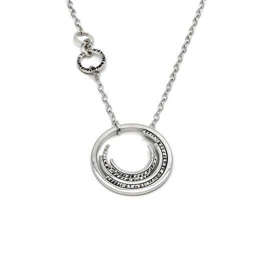 Contemporary sterling silver necklace with a prominent outer circle surrounded by five descending, staggered inner circles. The inner circles showcase varying textures, some chisel-textured and blackened for enhanced visual contrast. Suspended from a sterling silver cable chain, the pendant is complemented by four irregularly sized and textured rings positioned 1.5 inches up the chain on the right side
