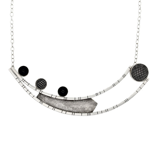 Necklace crafted from two long curved square wires with random black lines, connected at one end and split at the other. An angular sheet of blackened textured silver is positioned between the wires. On the right side of the top curved bar, three 10-millimeter stones are set – two black onyx and one silver mesh dome. On the left side, suspended between the ends of the curved bars, is a large bezel made of domed silver mesh. The pendant is attached to a link-in-link chain.