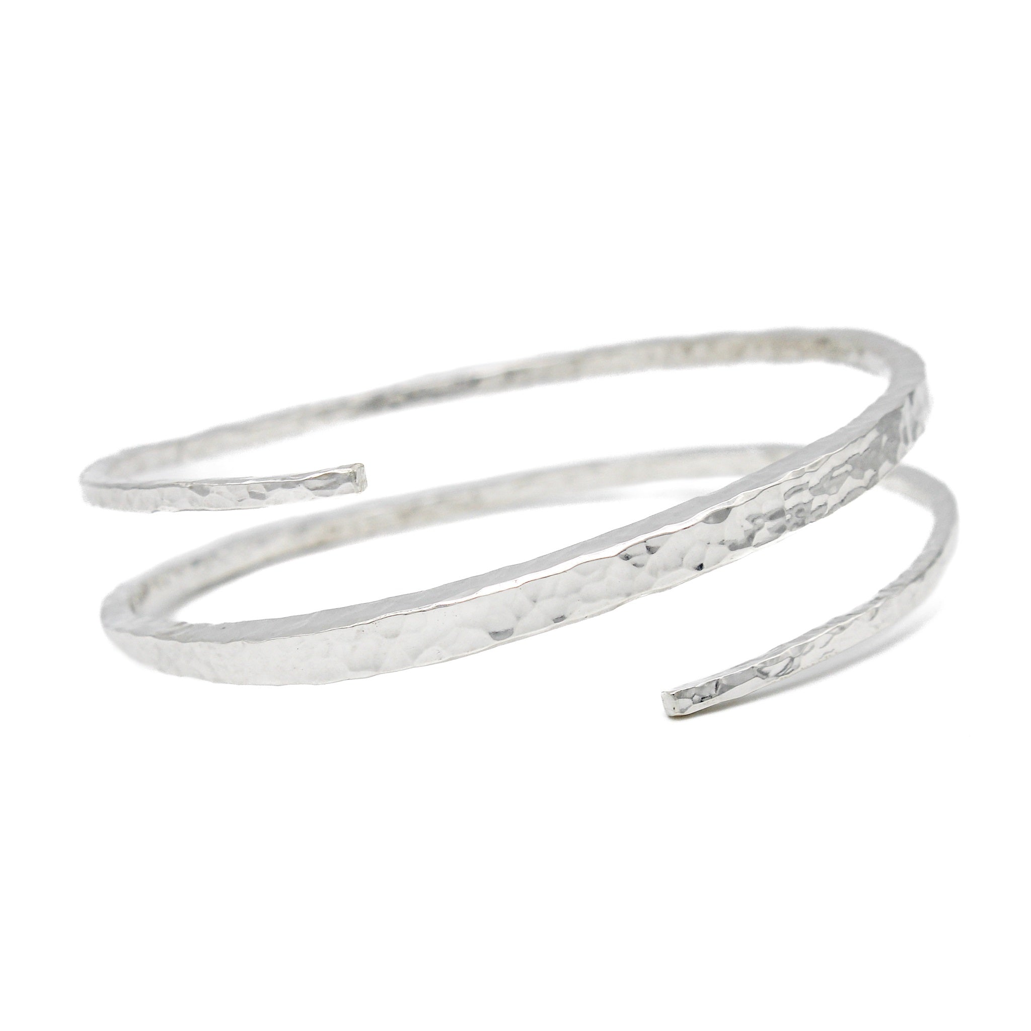 Sterling silver bracelet with a hammered texture. The bangles ends bypass eachother and create a single coil.  It is thicker in the middle and tapers towards either end. Bracelet is on a white background and facing forward